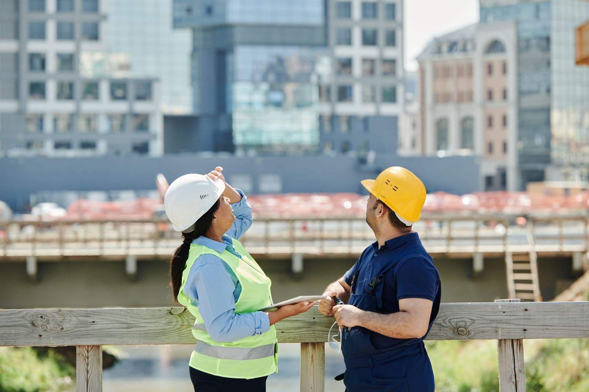 Engenheiros analisando plantas em canteiro de obras com a cidade ao fundo
